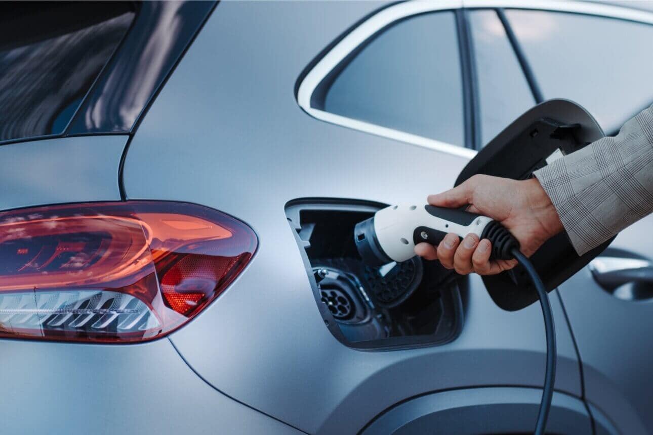 Man holding power supply cable at electric vehicle charging station.