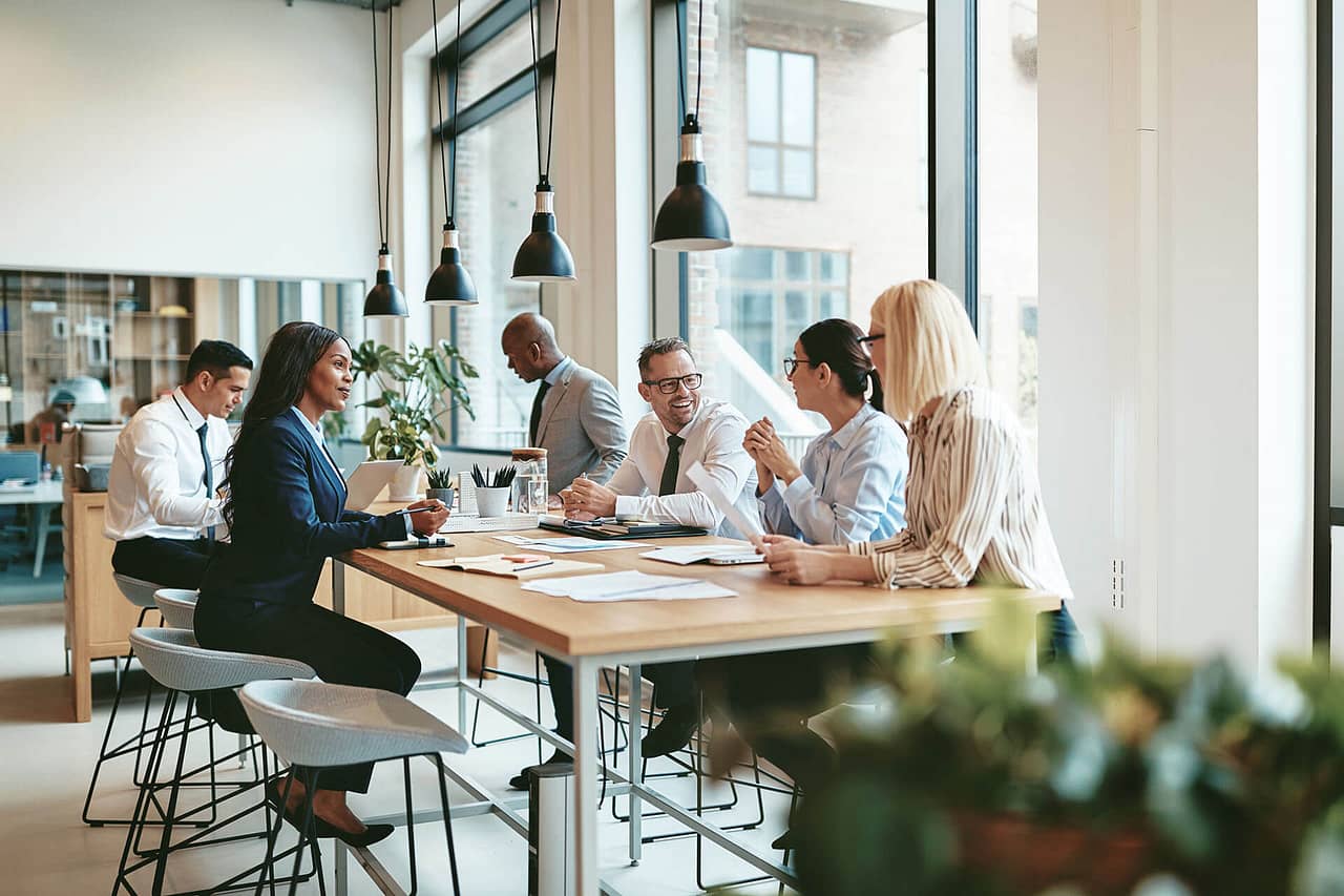 Smiling group of diverse businesspeople discussing paperwork together while having a meeting around a table in a modern office.